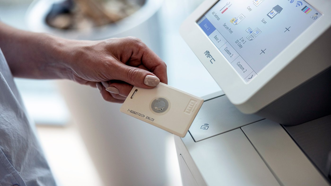 A person holds an ID card against a Brother printer’s NFC reader to authenticate before printing.