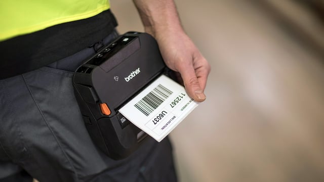Close up of a worker holding a Brother mobile label printer printing a barcode label.