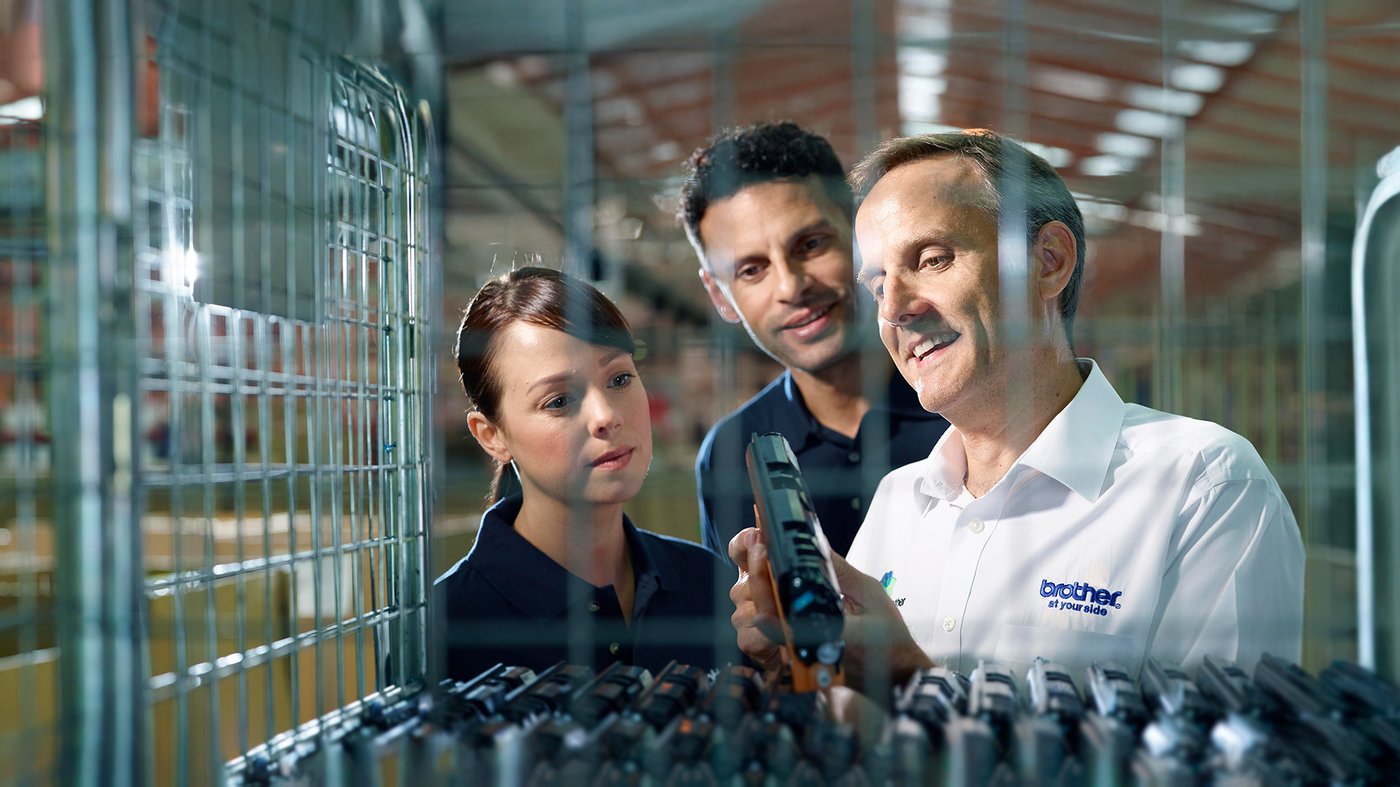Team inspecting and discussing a Brother printer component inside a manufacturing facility.