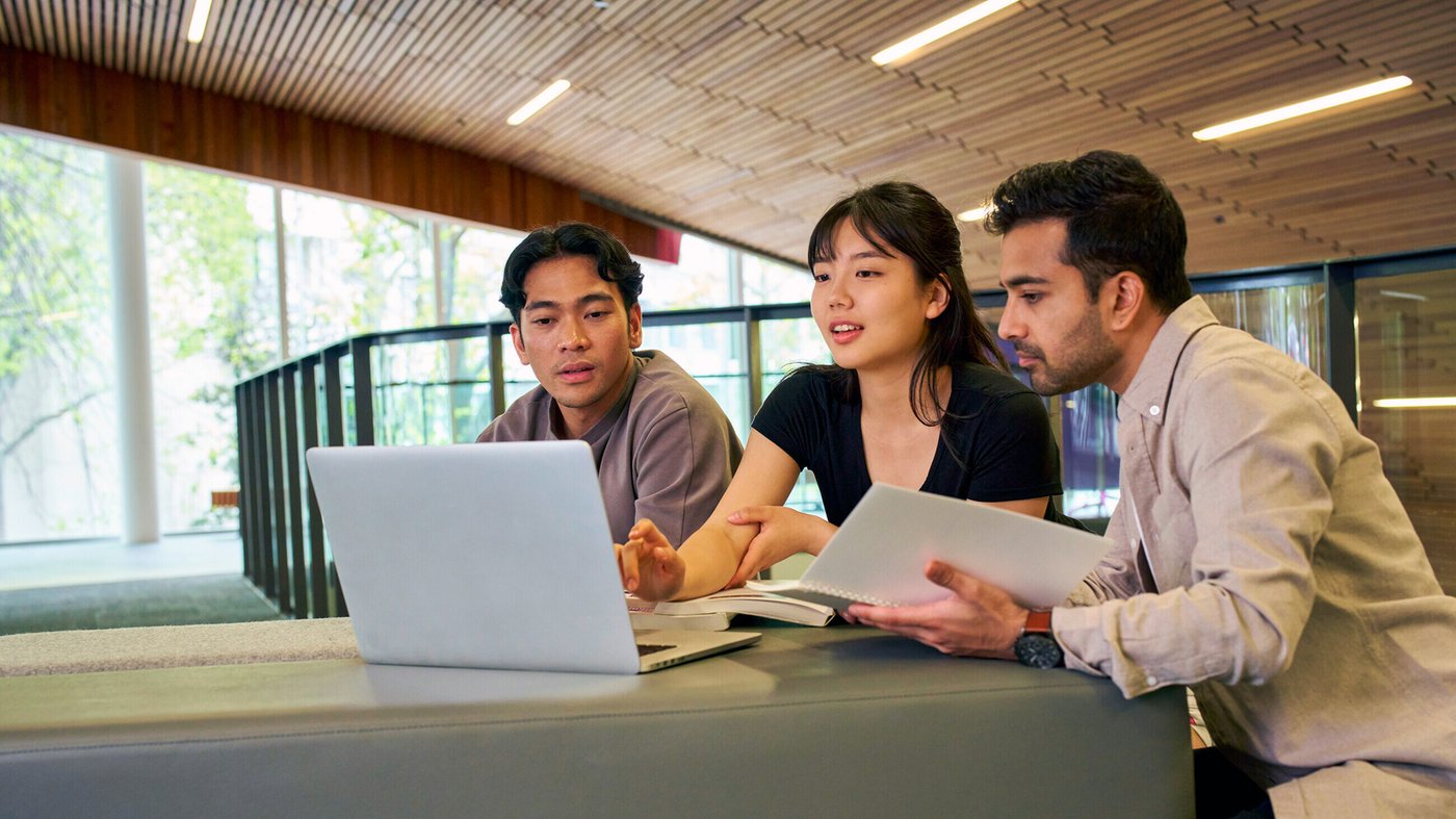 A group of tertiary students sitting together indoors, collaborating as they look at a laptop screen.