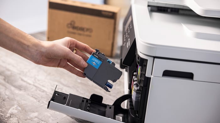 Hand removing an empty Brother ink cartridge from a printer as part of cartridge recycling.