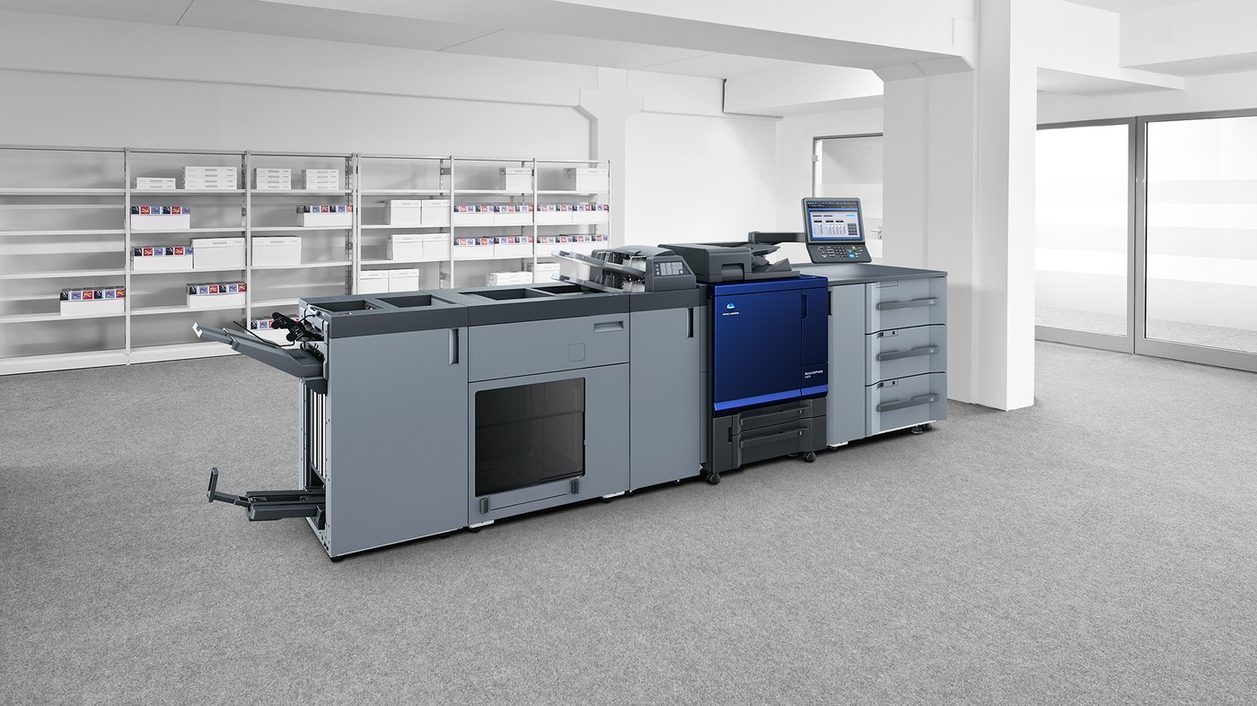 Large professional Konica Minolta AccurioPress C4070 production printer in a modern office space with shelves in the background.