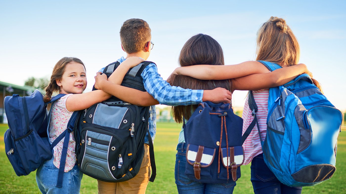 Group of school children with backpacks walking together with their arms around each other outdoors.