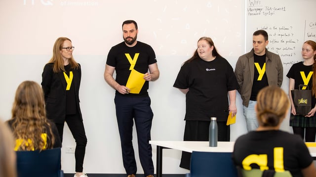Youth Innovator Awards presenters standing at the front of a classroom speaking to students.