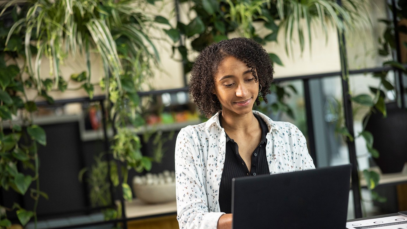 Employee working on a laptop in a modern office setting surrounded by plants.