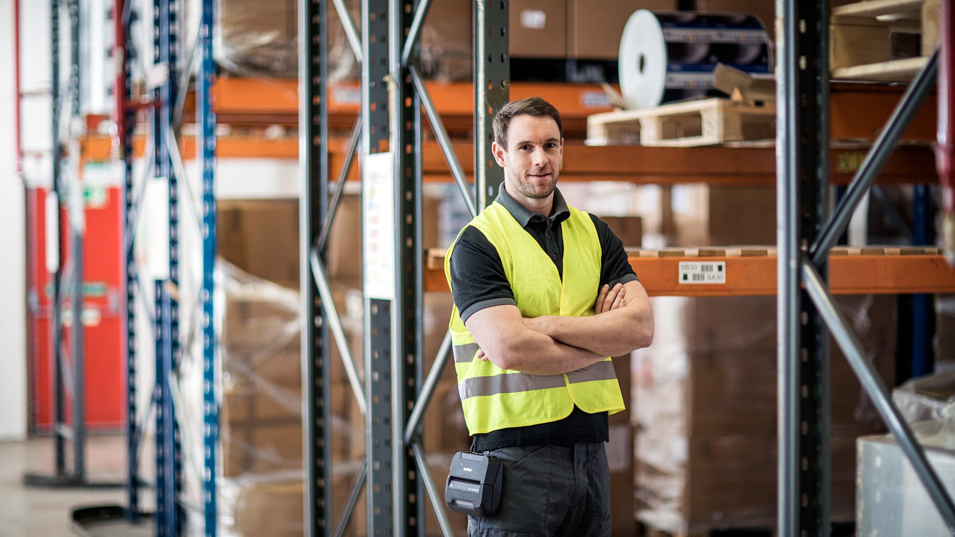 Warehouse staff member standing in a storage facility wearing safety gear.