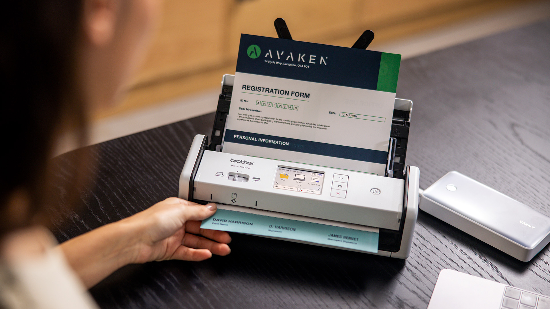 Person scanning a registration form using a compact Brother document scanner on a desk.
