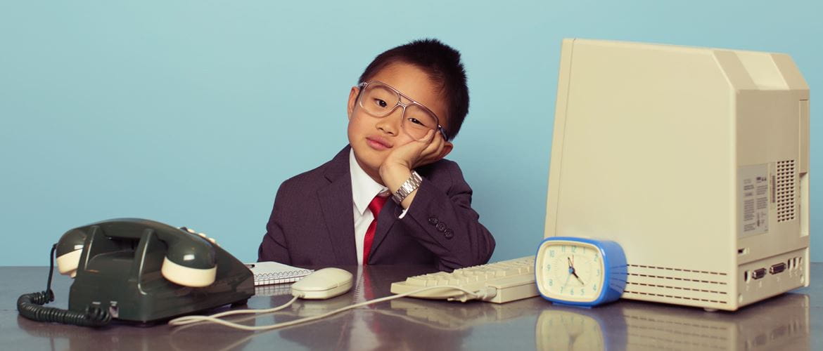 young boy businessman sits behind desk with retro technology on it
