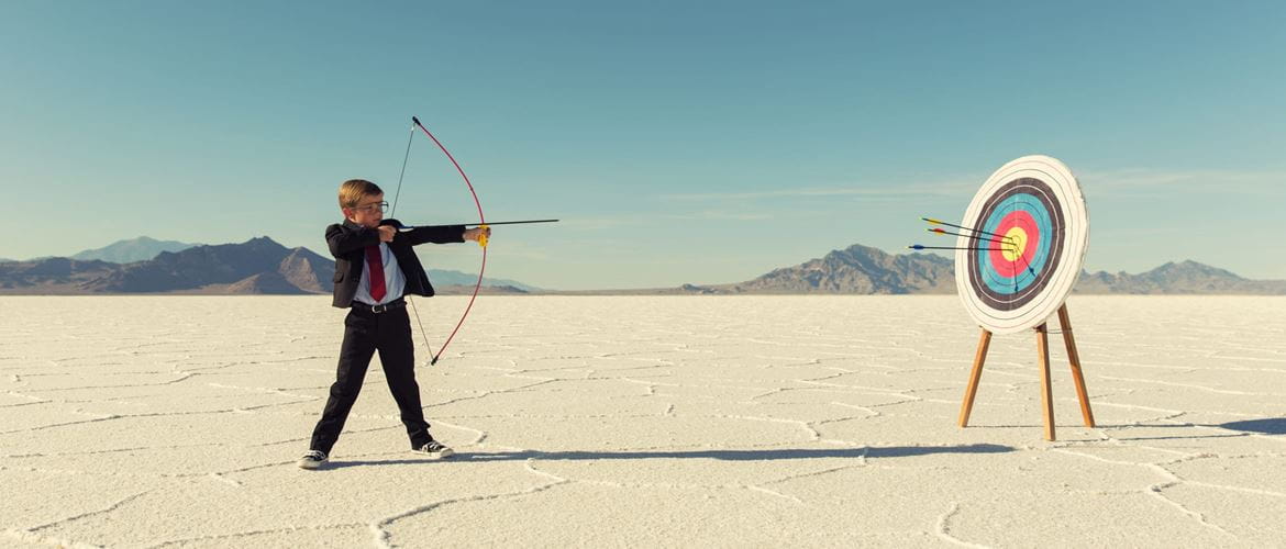 Young boy in a suit takes aim at a target with a bow and arrow