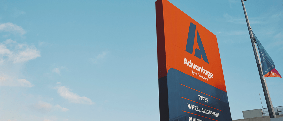 A tall signboard against a blue sky with some clouds, displaying the logo and services of 