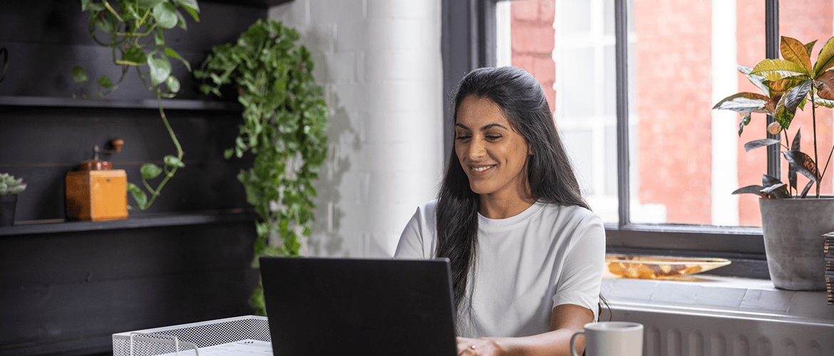 a woman sitting at a desk in an industrial style office up close looking at a laptop happy