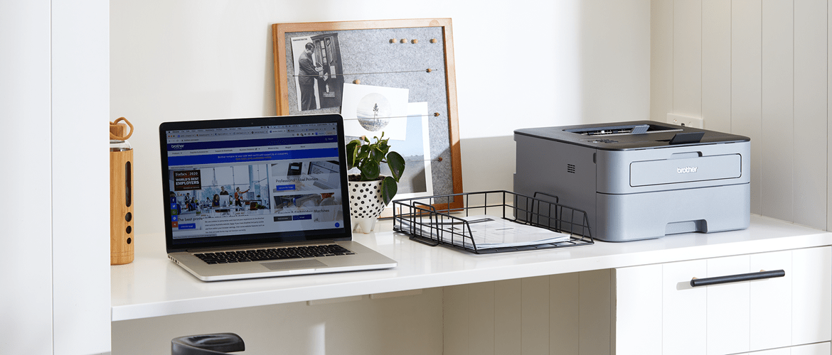 a modern home desk with laptop and printer to represent Brother's quality policy