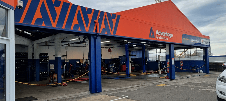 Exterior of Advantage Tyre Solutions garage with open service bays, blue and orange branding, visible tire service equipment, and company signage.