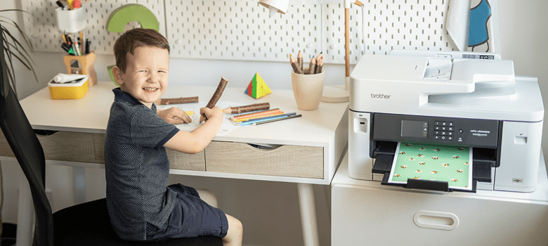 a child sitting at a desk with a pencil looking happy sitting next to a printer