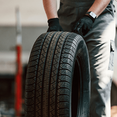 Mechanic in uniform and gloves holding a car tire in an auto repair shop, showcasing managed printing solutions by Brother.