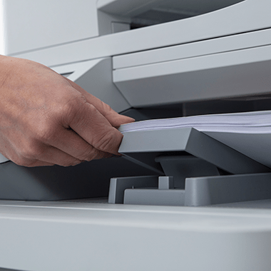 Close-up of a hand placing paper into a printer tray, highlighting managed print services by Brother.
