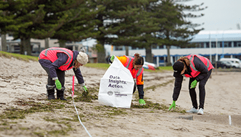 three people picking up litter on a beach wearing high-visibility vests