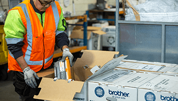 a man wearing a high-visibility vest unboxes a large recycling box and removes a toner cartridge with his hands